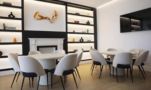 Un comedor moderno con una mesa y sillas blancas, una chimenea y estanterías con diversos objetos.
