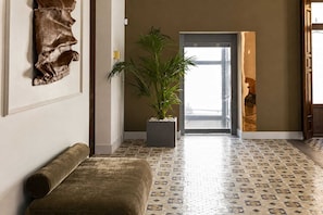 Un pasillo con suelo estampado, un banco, una planta en maceta y una puerta que da a otra habitación.