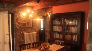 Uma sala de jantar acolhedora com uma mesa de madeira, cadeiras, um cesto de frutas, uma estante e uma parede de pedra.