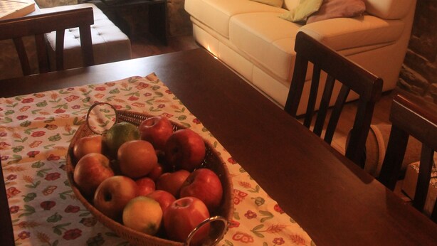 Uma sala de estar acolhedora com parede de pedra, um sofá branco, uma mesa de madeira e uma fruteira.