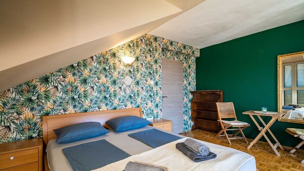 Ein Schlafzimmer mit einem Bett, einem Nachttisch aus Holz, einer Kommode, einem Sessel, einem Tisch und einem Spiegel.