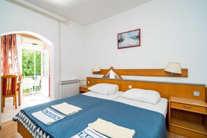 Ein Hotelzimmer mit Bett, Nachttischen, Heizkörper, einem mit Vorhängen versehenen Fenster und einem Bild an der Wand.