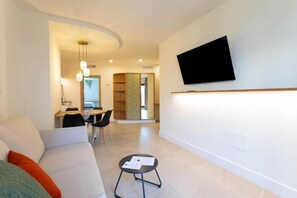 Un salon moderne avec un canapé, un coin repas avec des chaises, une petite table avec des papiers et un téléviseur fixé au mur.