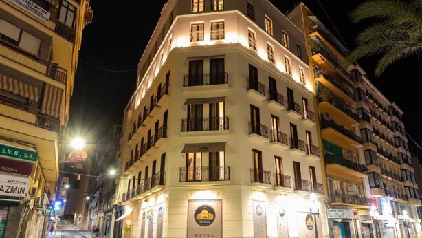 A multi-story hotel with balconies, illuminated signage, and a street view.