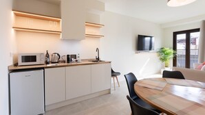 A modern kitchen with a microwave, kettle, and coffee maker, a dining area with a table and chairs, and a TV mounted on the wall.