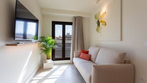 A modern living room with a sofa, a flat-screen TV, a potted plant, and a city view through the window.