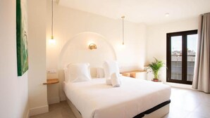 A hotel room with a large bed, bedside tables, a potted plant, and a view through a sliding door.