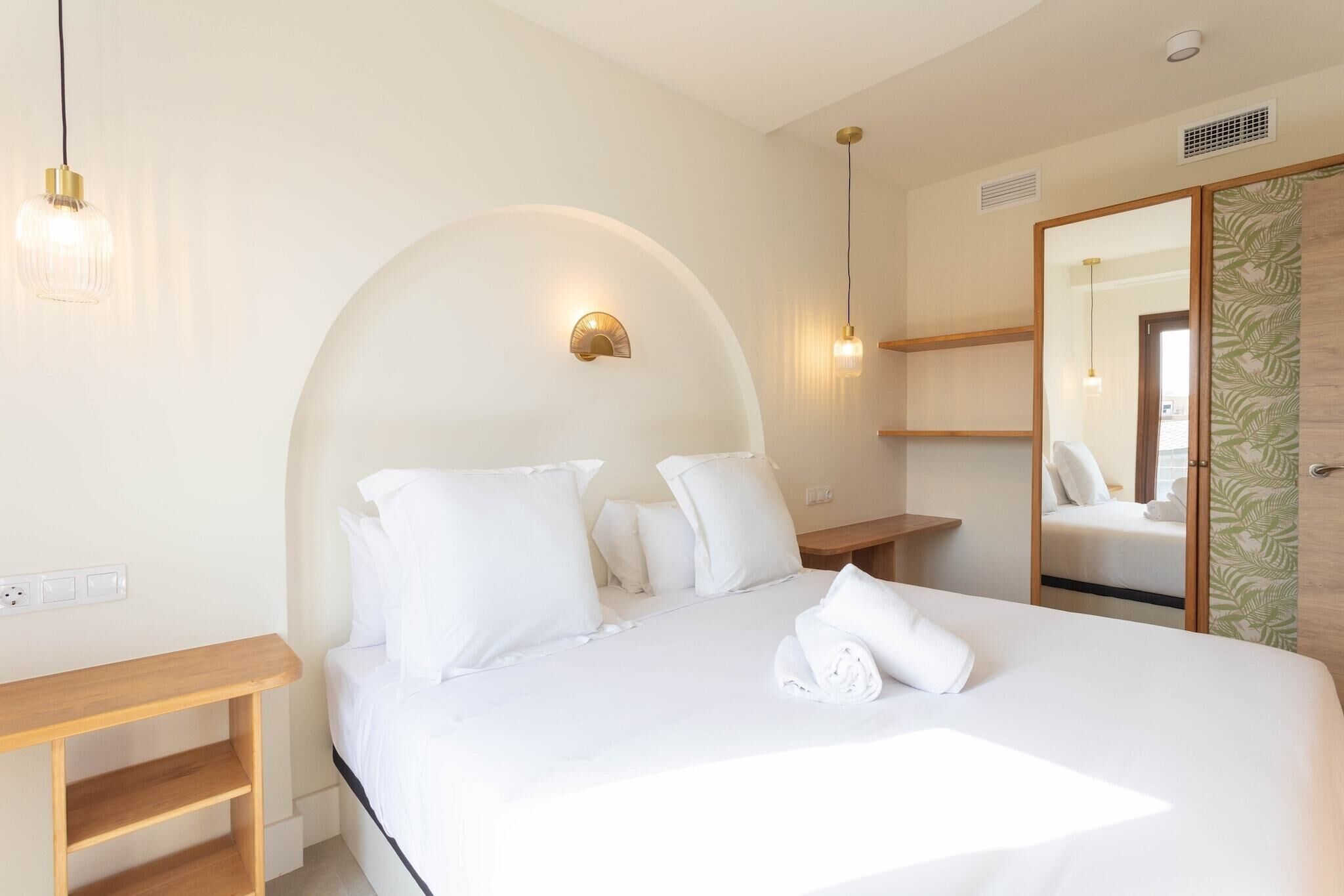 Habitación de hotel con una cama grande, una mesita de noche de madera, una lámpara de pared y un espejo.