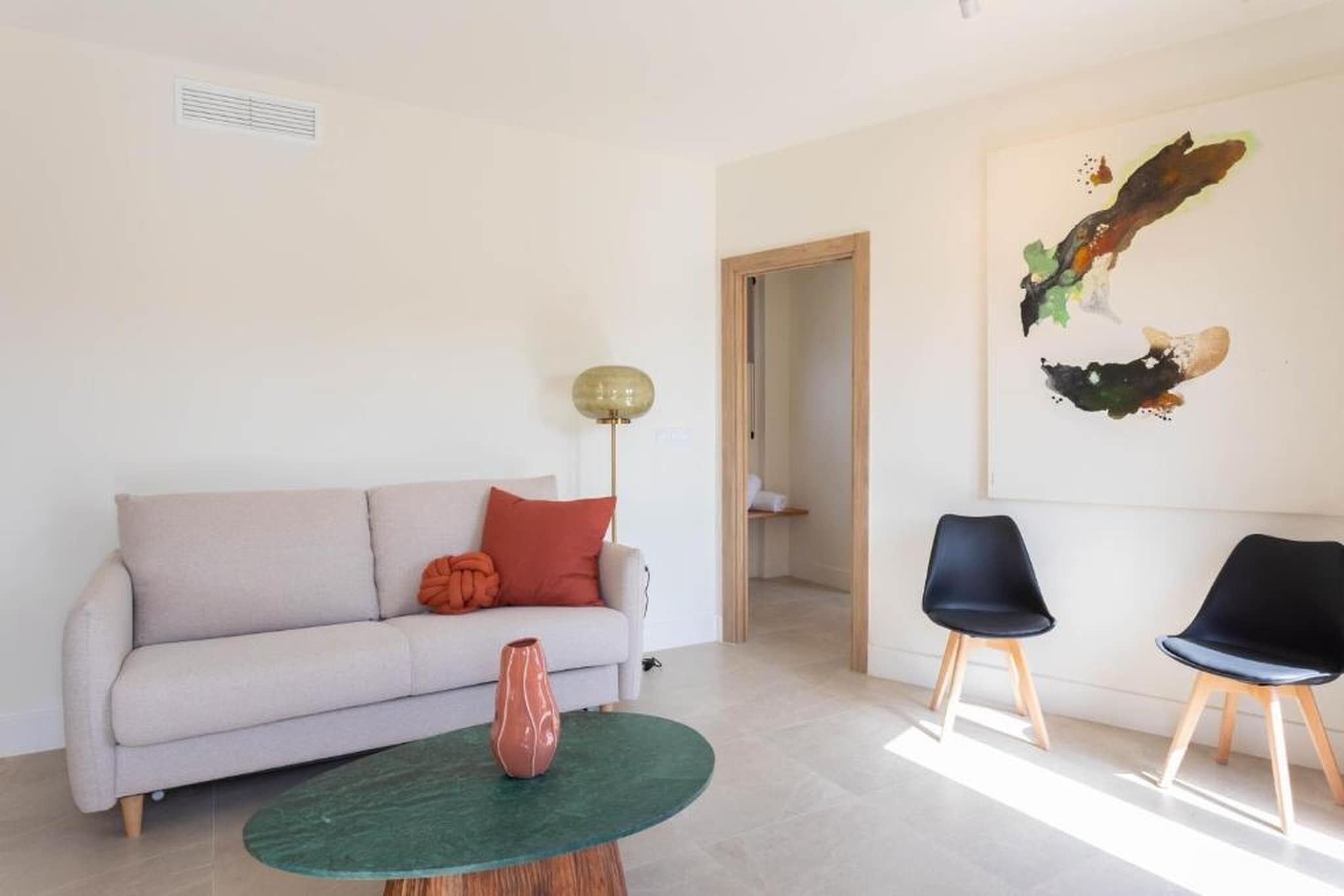 Una sala de estar con un sofá, una mesa redonda, dos sillas, una lámpara de pie y un cuadro en la pared.