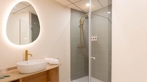 A bathroom with a round mirror, a white sink, a glass-enclosed shower, and a wooden vanity.