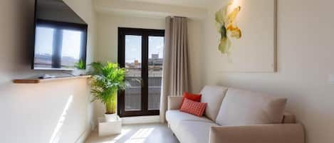 Un salon moderne avec un canapé, un téléviseur à écran plat, une plante en pot et une vue sur la ville par la fenêtre.