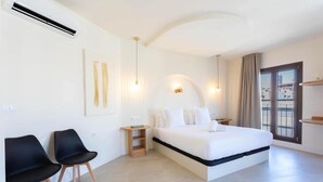 A modern hotel room with a large bed, two black chairs, a small wooden side table, and a large window with a view. - Deluxe quadruple apartment (Alicante)