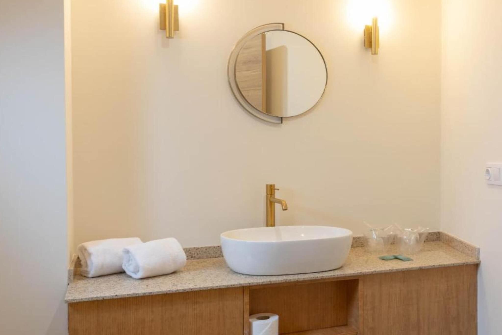 A bathroom with a round mirror, a white sink, and two towels on the counter.