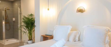 A hotel room with a bed, a bedside table, a nightstand, a potted plant, and a shower area.