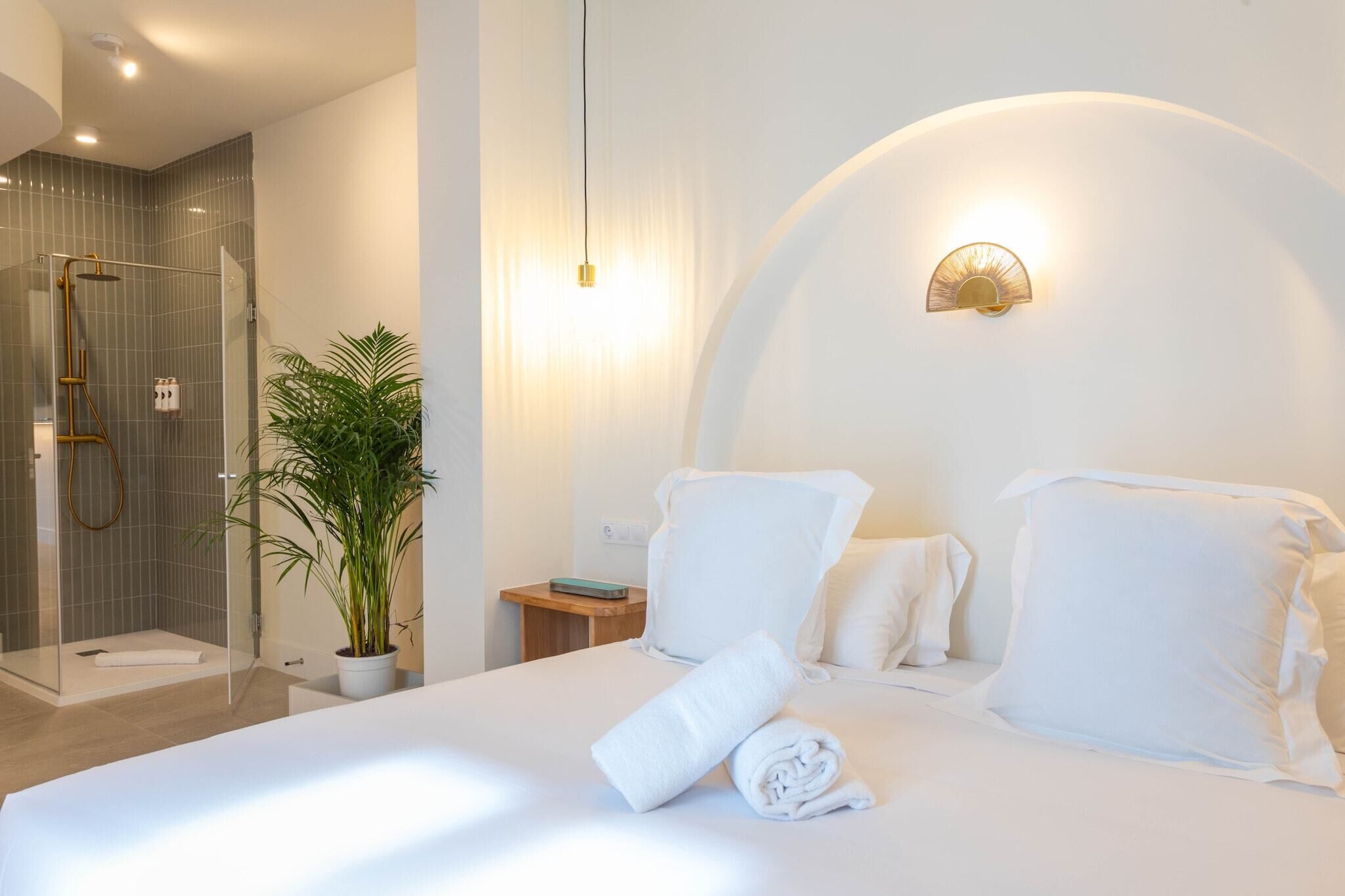 Une chambre d’hôtel comprenant un lit, une table de chevet, une petite table, une plante en pot et un espace douche.