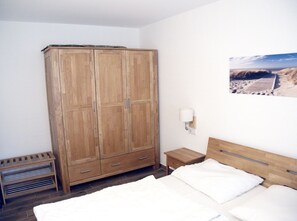 Ein Schlafzimmer mit Holzschrank, Nachttisch, Bett mit weißer Bettwäsche und einer Wandlampe.