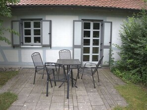 Eine Terrasse mit Tisch und Stühlen, ein Fenster mit Rollläden und eine Tür mit Glasverkleidung.