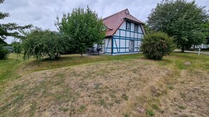 A traditional half-timbered house with a red roof, surrounded by a grassy area and trees. - Vacation Rental on Nordstrand—Close to the Beach and Comfortable—Comfortable (Dranske)