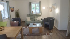 A living room with a sofa, chairs, a coffee table, and a window with curtains. - Vacation Rental on Nordstrand—Close to the Beach and Comfortable—Comfortable (Dranske)