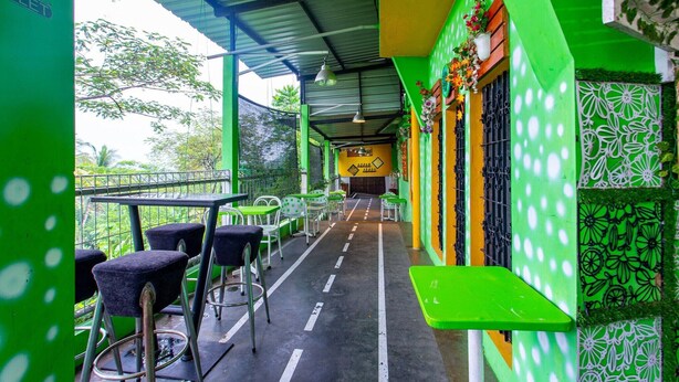 An outdoor seating area with tables and chairs, a covered walkway, and a view of the surrounding greenery.