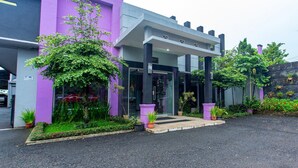 A modern building with a purple facade, a covered entrance, and a well-maintained garden area.