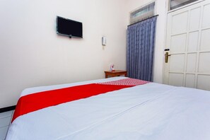 Hotelkamer met een bed, een aan de muur bevestigde televisie, een telefoon en een raam met gordijnen.