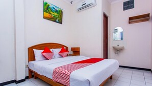 A hotel room with a bed, a painting, an air conditioning unit, a mirror, and a sink.