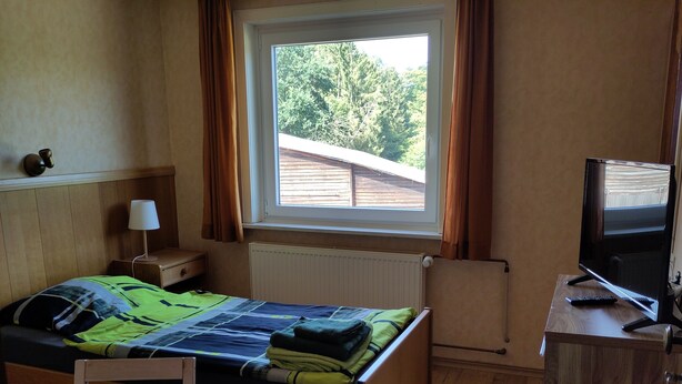 Un dormitorio con cama, escritorio, televisor y ventana con cortinas.