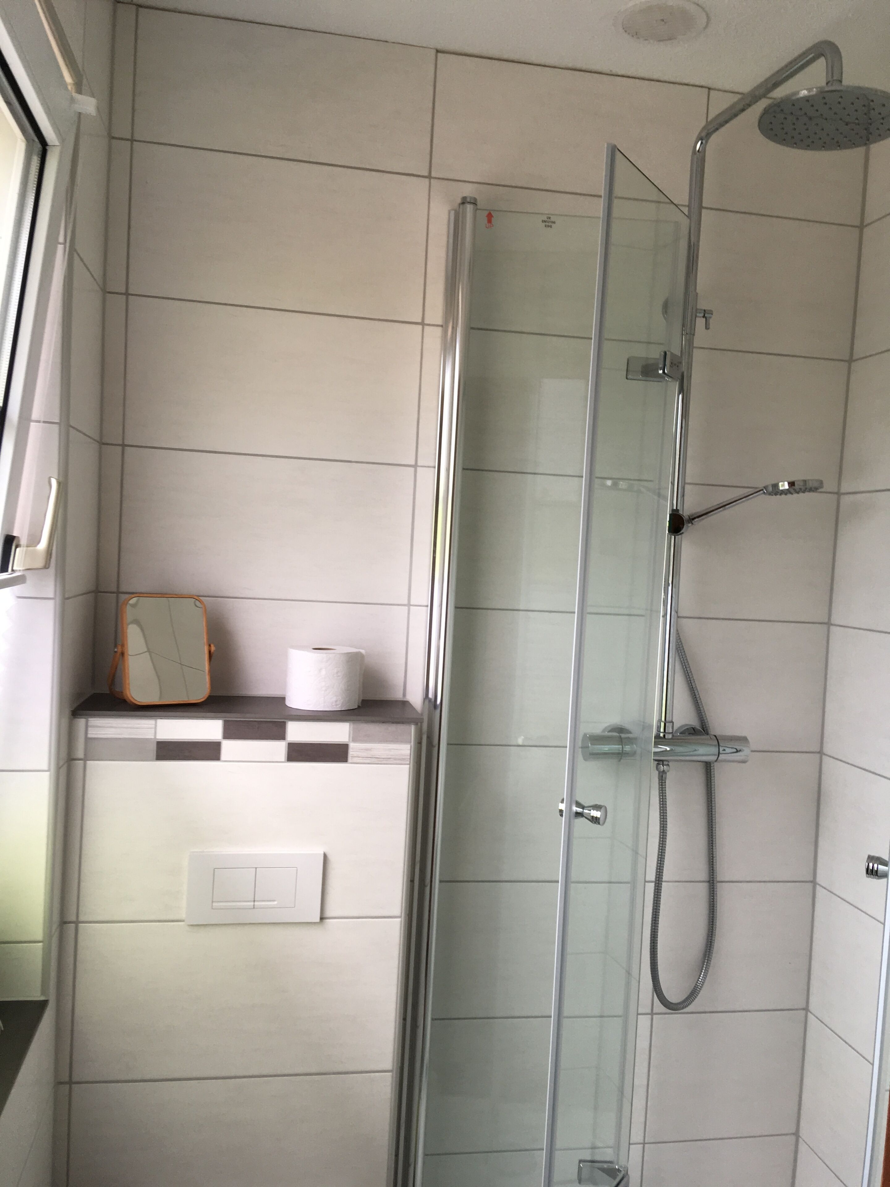 Ducha envuelta en vidrio con cabezal de ducha manual y grifo de mano.