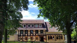 Un edificio tradicional de entramado de madera con una entrada central, un pequeño porche y un jardín amurallado.