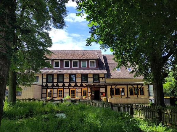 A traditional half-timbered building with a central entrance, a small porch, and a fenced garden area.