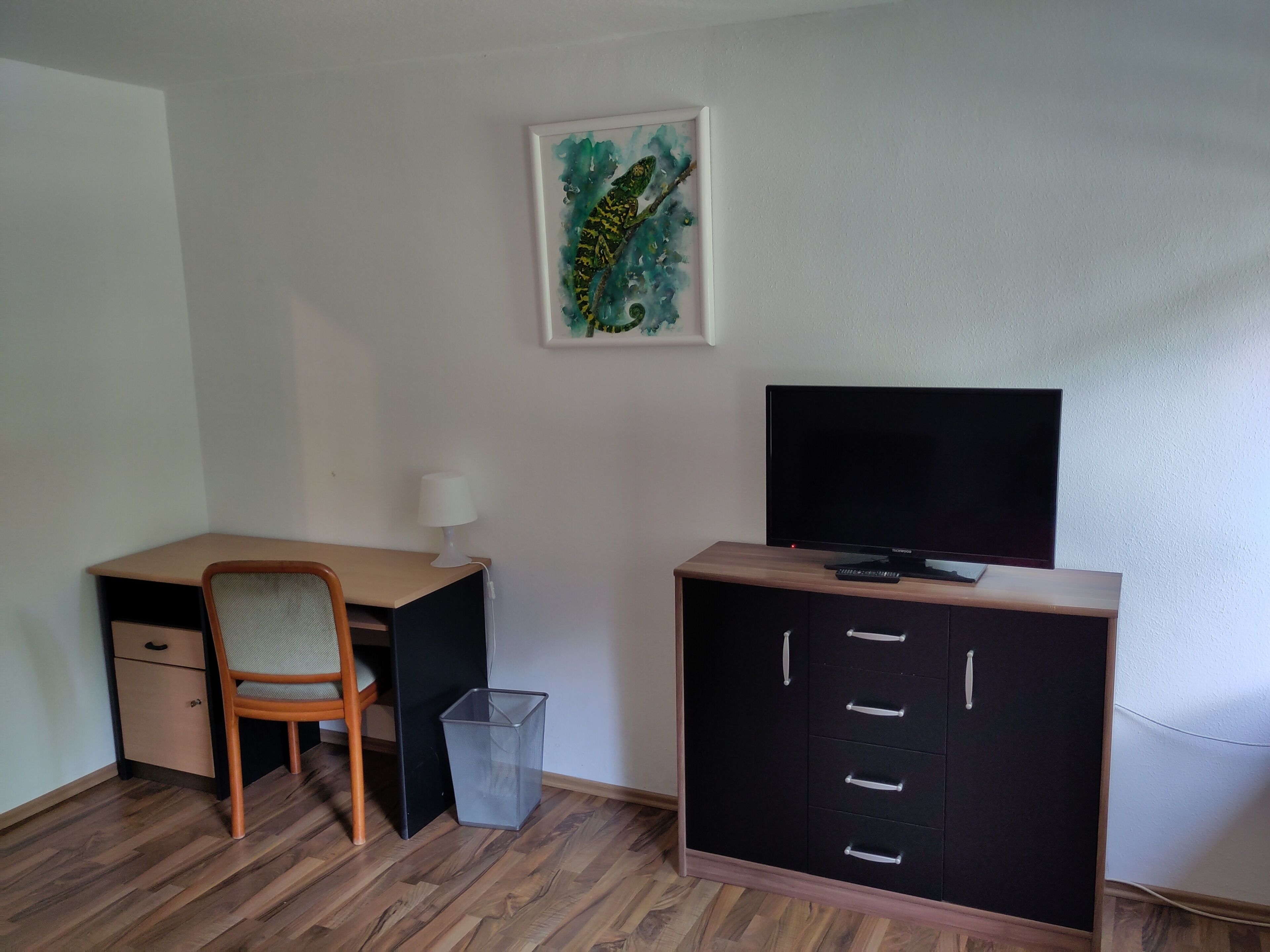 Een kamer met een houten bureau, een stoel, een televisie en een dressoir met lades.