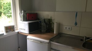 Una cocina compacta con microondas, cafetera y lavamanos.