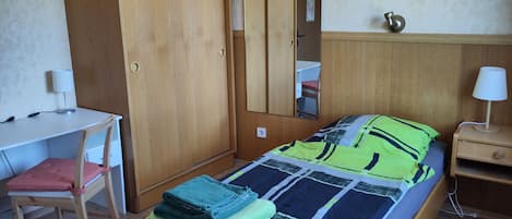 A bedroom with a bed, a desk, a chair, a wardrobe, and a bedside table.