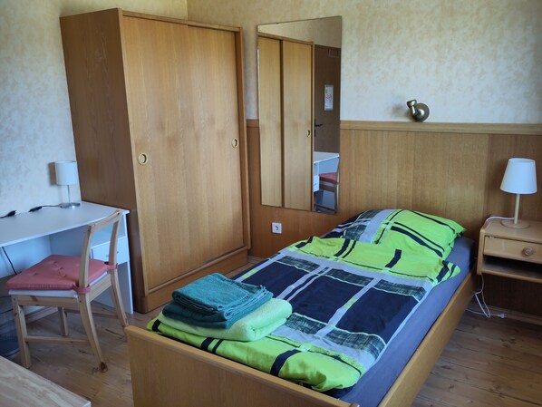 A bedroom with a bed, a desk, a chair, a wardrobe, and a bedside table.