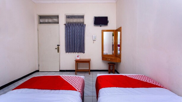 Quarto de hotel com duas camas, uma porta, uma mesinha, um espelho e uma televisão na parede.
