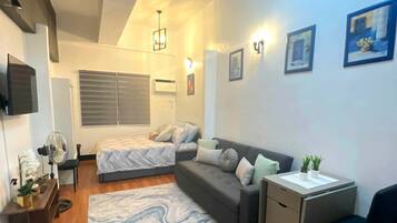 A compact living space with a bed, sofa, desk, and a small kitchenette.