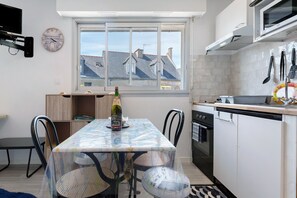 A compact kitchen with a dining table, chairs, a microwave, and a window with a view of buildings.