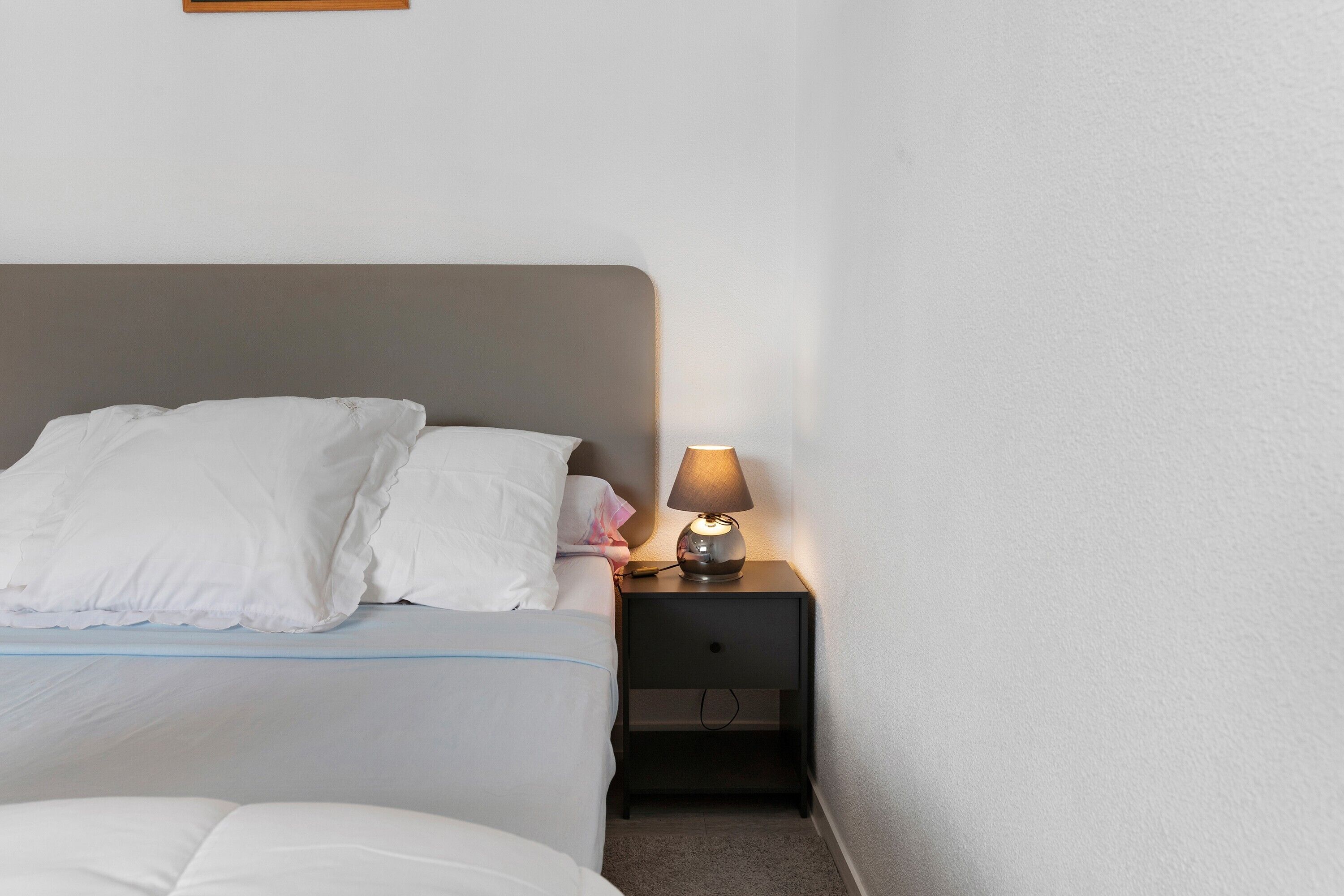 Un lit bien fait, avec du linge de lit blanc et une tête de lit grise, dans une chambre d’hôtel.