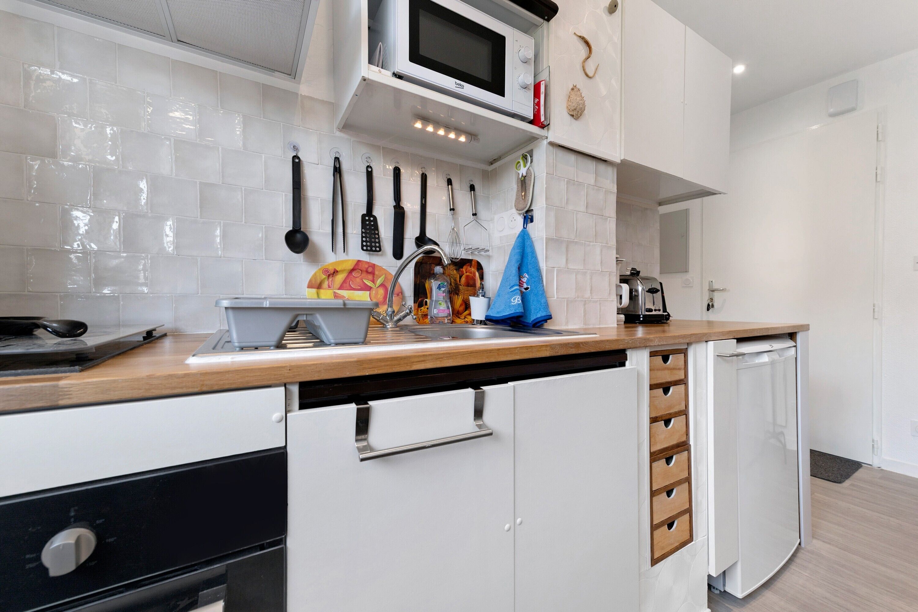A modern kitchen with white cabinets, a microwave, and various utensils hanging on the wall.