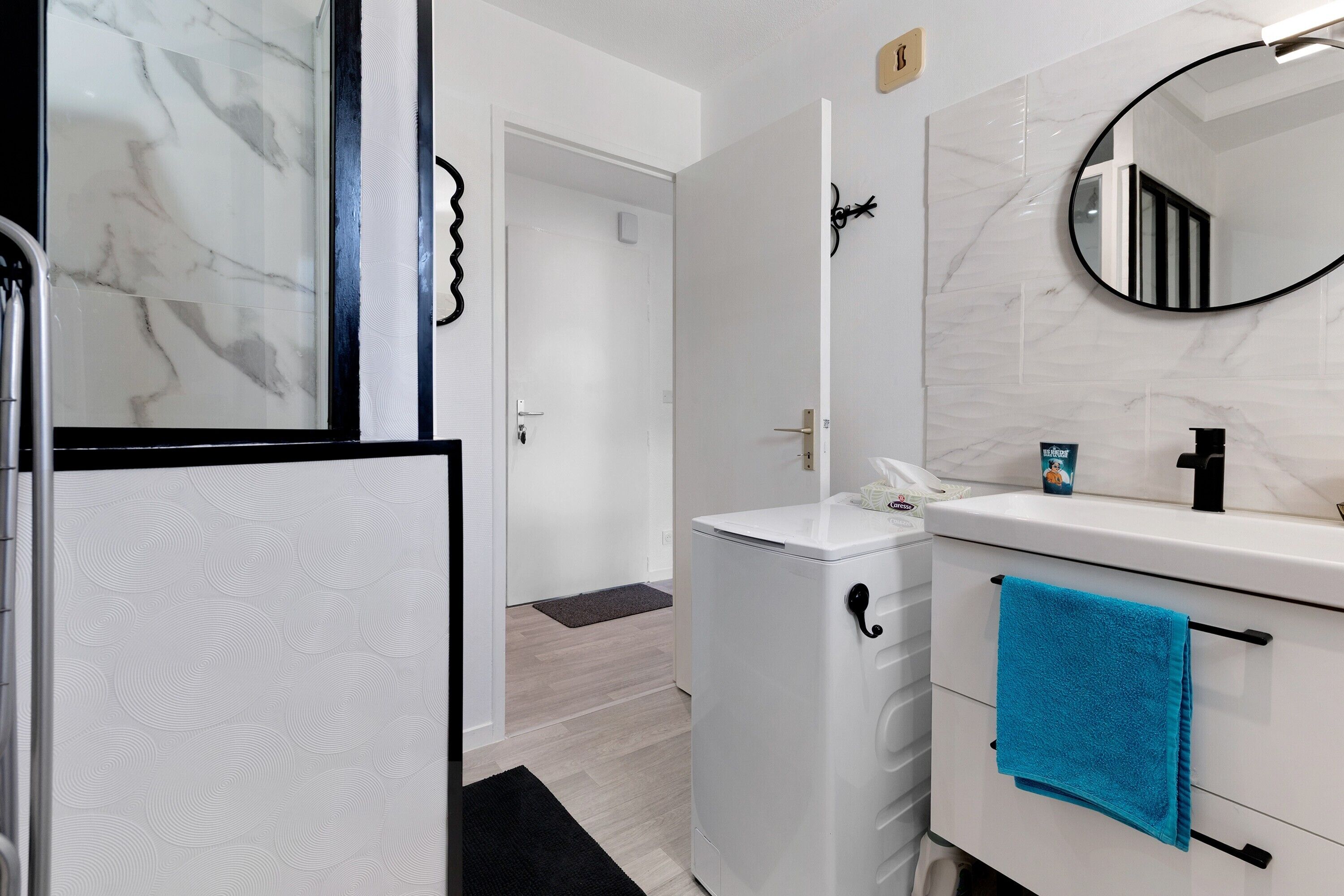 A bathroom with a white marble wall, a white sink with a black faucet, a blue towel, and a white toilet.