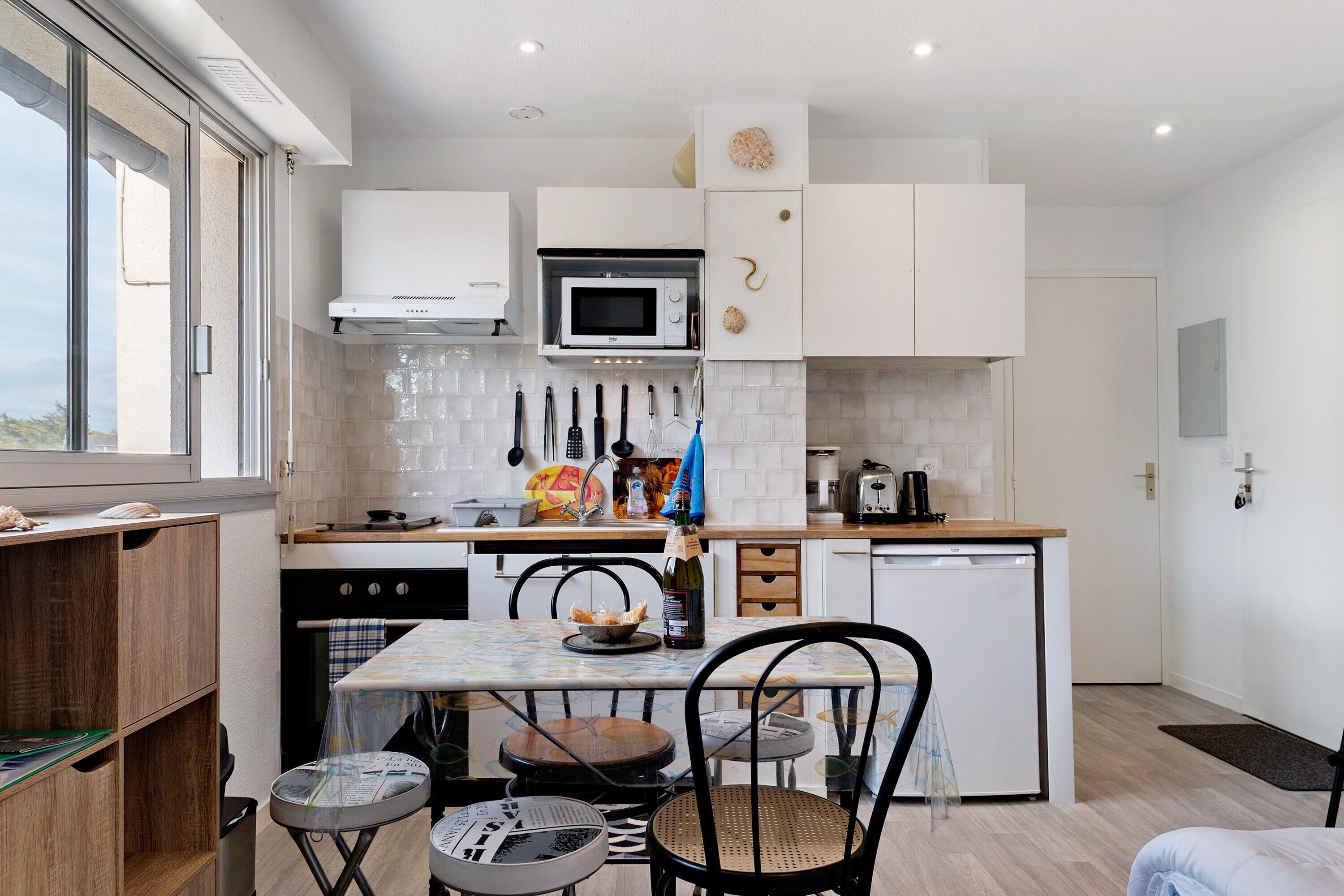 Una cocina compacta con armarios blancos, un microondas y un pequeño comedor con mesa y sillas.