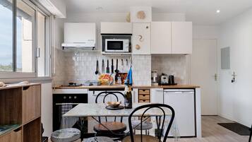 Una cocina compacta con armarios blancos, un microondas y un pequeño comedor con mesa y sillas.