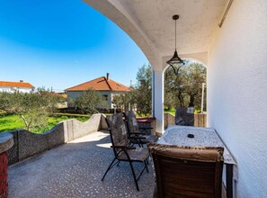 Eine Terrasse im Freien mit Tisch und Stühlen, Blick auf ein Haus und einem klaren Himmel.