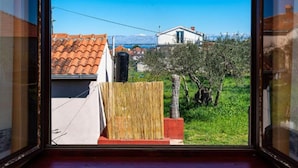 A view from a window overlooking a residential area with a house, a tree, and a clear blue sky. - Two Bedroom Apartment With Terrace (Preko)