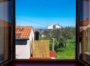 Blick aus einem Fenster auf ein Wohngebiet mit einem Haus, einem Baum und blauem Himmel.