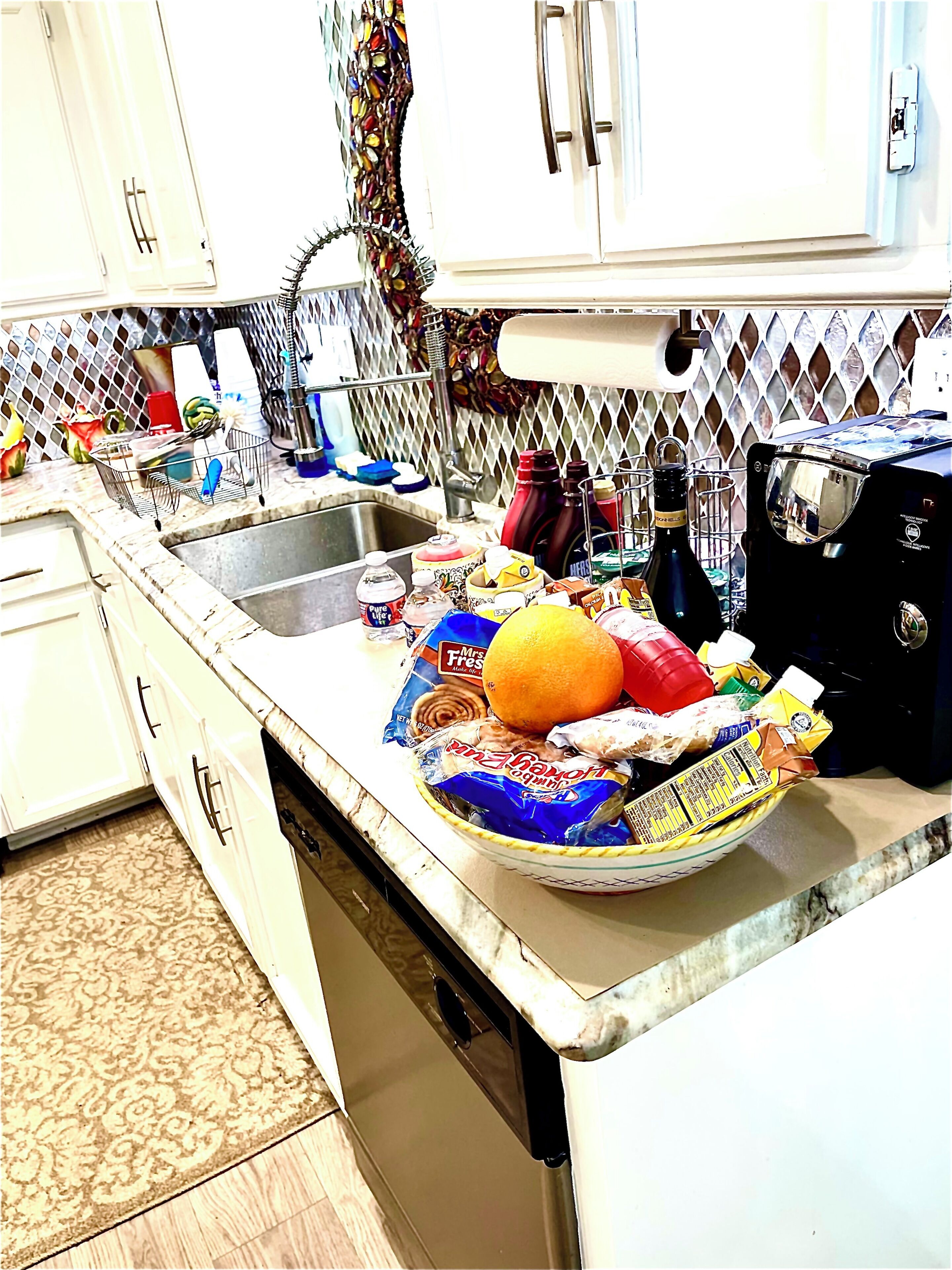 A kitchen with a sink, countertop, and various food items.