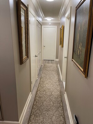 Un couloir avec un tapis à motifs, des portes blanches et des œuvres d’art encadrées accrochées aux murs.