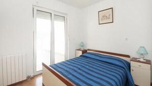 A bedroom with a bed, a nightstand, a lamp, a radiator, and a sliding door to a balcony. - Bertie's Lodge - Two Bedroom Apartment With Terrace and Sea View (Smokvica)