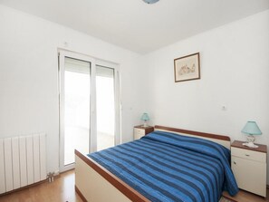 A bedroom with a bed, a nightstand, a lamp, a radiator, and a sliding door to a balcony. - Bertie's Lodge - Two Bedroom Apartment With Terrace and Sea View (Smokvica)